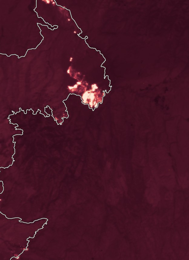 Mid-wave infrared FireSat image of the Big Grass Fire, with bright hotspots glowing along the edge of the white fire perimeter line against a dark maroon landscape.